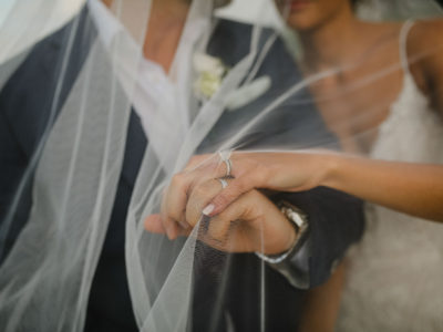 wedding rings photographed under the vale while bride and groom holding hands