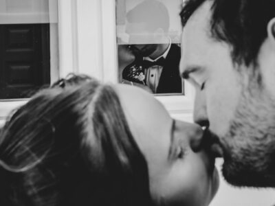 Mykonos kiss, a couple kissing photographed from behind while their faces are noticeable at a windows reflection. Shoot in black and white format.